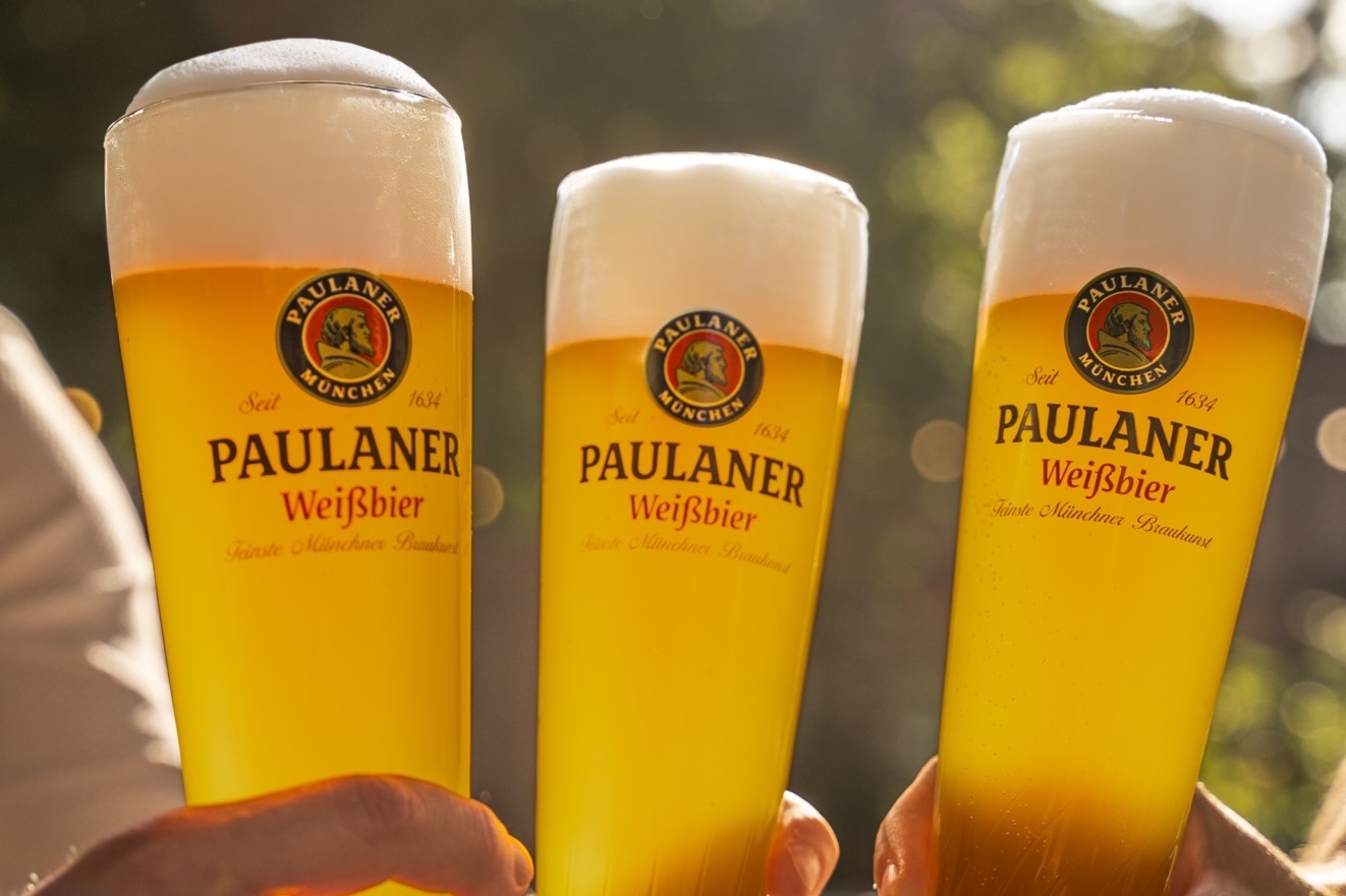 Drei Gläser Paulaner Weißbier mit Schaumkrone stehen im Vordergrund.